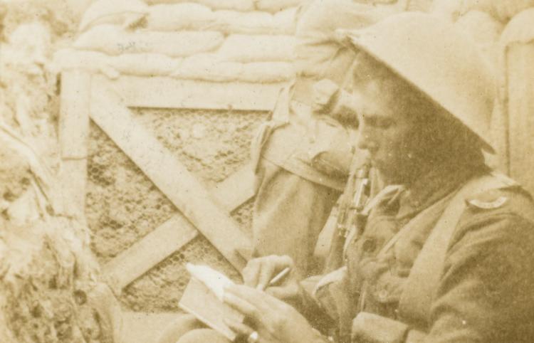 A solider sits in a trench rolling a cigarette 