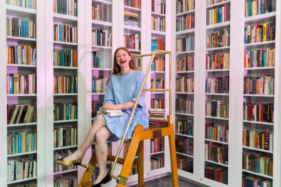A person sits on a ladder in front of walls of books