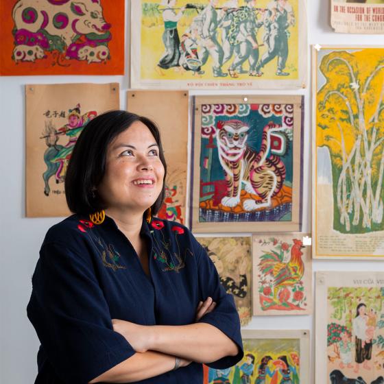 A woman stands in front of Vietnamese posters, smiling.