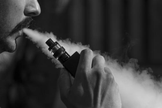 Black and white photograph of man blowing vapour out of a vape pen